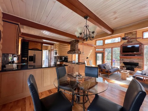 Cozy log cabin interior featuring a dining table, kitchen, and living area with large windows and rustic decor.