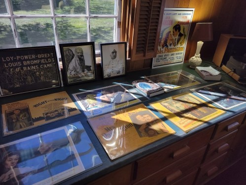 A display of vintage movie posters and framed photos on a table in a well-lit room with wooden furnishings.