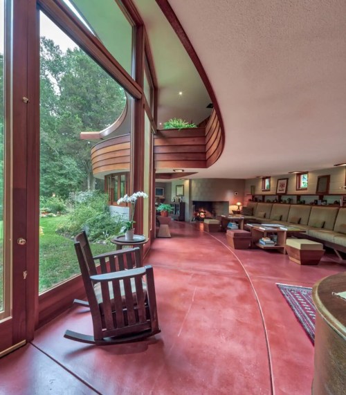 A modern interior with large windows, curved wood accents, and a cozy seating area overlooking a garden.