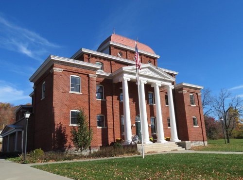 Historic brick building with white columns, a red roof, and an American flag, set against a clear blue sky.