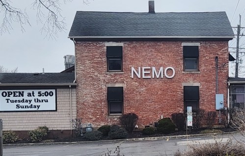 A brick building with the word "NEMO" on the front, and a sign indicating it's open at 5:00 PM, Tuesday to Sunday.