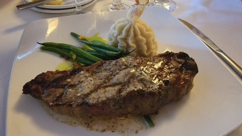 A plate featuring a grilled steak, mashed potatoes, and green beans, elegantly presented on a white dish.