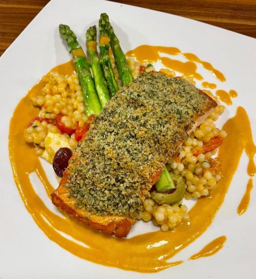 A plated dish featuring herb-crusted salmon, asparagus, and couscous drizzled with a creamy sauce.