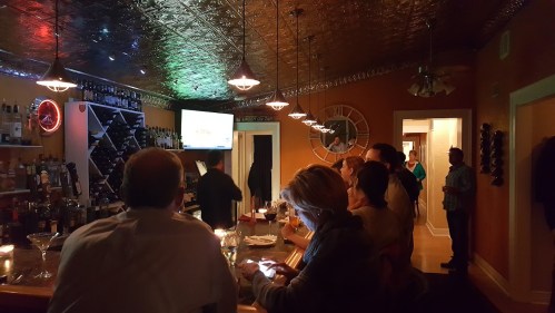 A cozy bar scene with patrons enjoying drinks, a bartender serving, and a TV displaying a game in the background.