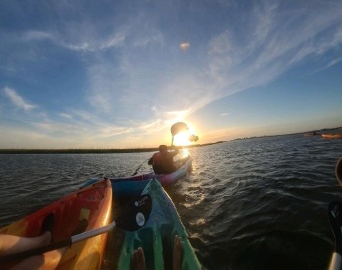 A sunset over water with kayakers paddling, creating a serene outdoor scene.