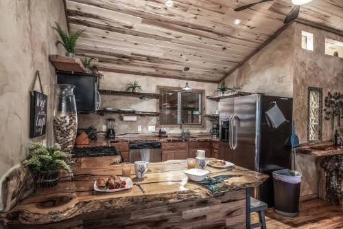 Cozy rustic kitchen with wooden accents, a large island, and a breakfast spread on the table. Natural light fills the space.