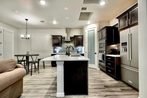 Modern kitchen with dark cabinets, a central island, stainless steel appliances, and a dining area with a table and chairs.