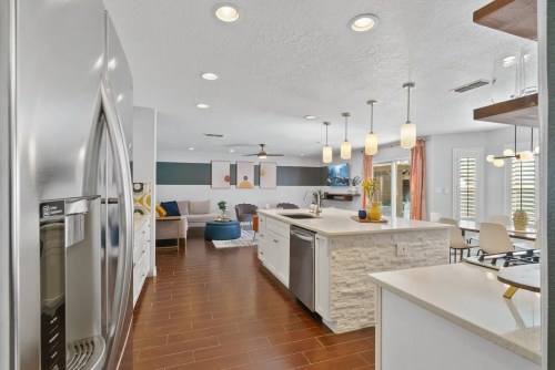 Modern kitchen with stainless steel appliances, an island, and a cozy living area in the background. Bright and inviting space.