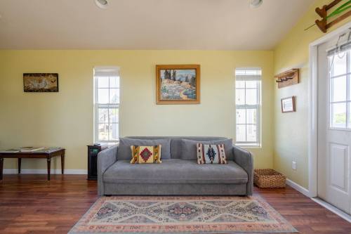 Cozy living room with a gray sofa, decorative pillows, a painting, and bright windows. Warm yellow walls and wooden floor.