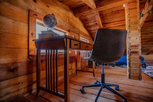 A wooden desk and chair in a cozy, rustic attic with wooden walls and a globe on the desk.