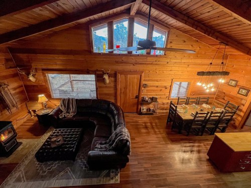 Cozy wooden cabin interior with a sectional sofa, dining area, and large windows showcasing a scenic view.