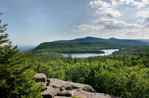A scenic view of a lush green landscape with a lake surrounded by mountains under a partly cloudy sky.