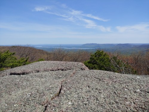 A rocky outcrop overlooks a vast landscape of rolling hills and a clear blue sky.