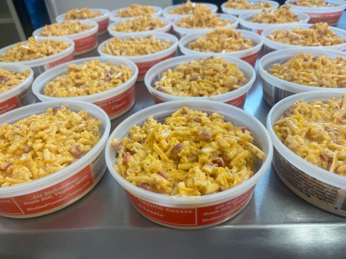 Containers filled with creamy macaroni and cheese, arranged neatly on a stainless steel surface.