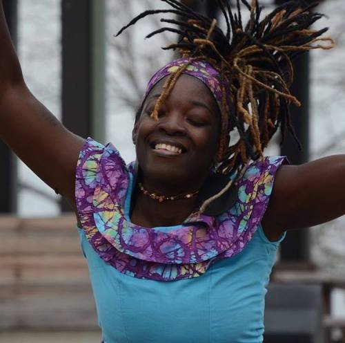 A joyful dancer with vibrant hair and a colorful outfit, smiling while performing outdoors.