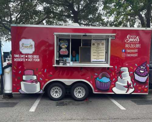 A colorful food truck named "Sassy Sweets" offering desserts like funnel cakes and fried Oreos, with a cheerful vendor inside.