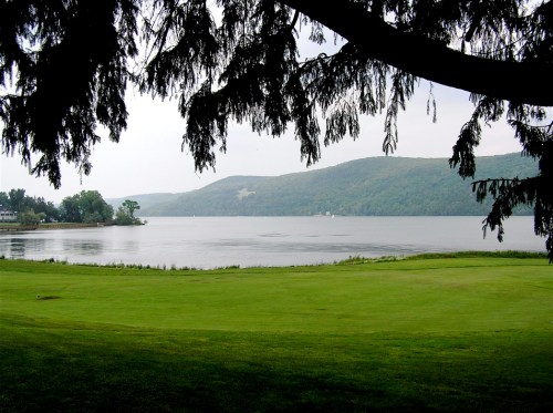 A serene lake view framed by tree branches, with rolling hills in the background and calm waters reflecting the sky.