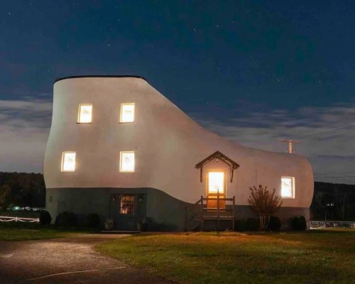 A whimsical shoe-shaped house illuminated at night, with windows glowing against a dark sky.