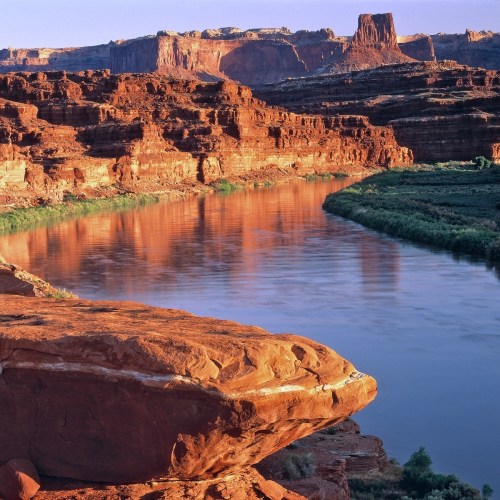A scenic view of a river winding through red rock formations under a clear blue sky.