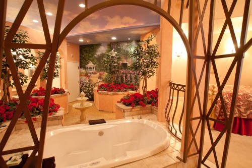 Luxurious bathroom with a large tub, floral decor, and a romantic garden mural, framed by an elegant archway.