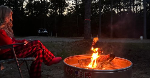 A camper wearing flannel red pajamas sits by a fire pit at a peaceful campground in PA.