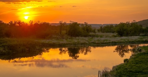 A vibrant golden sunset reflecting on the calm waters of the Pembina River in Walhalla, North Dakota.
