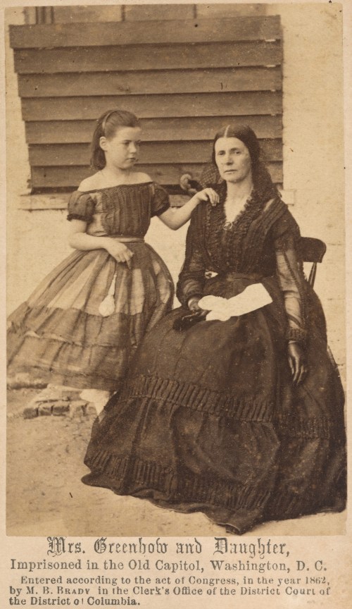 A woman and her daughter sit together, both in historical dresses, with a caption about their imprisonment in 1862.