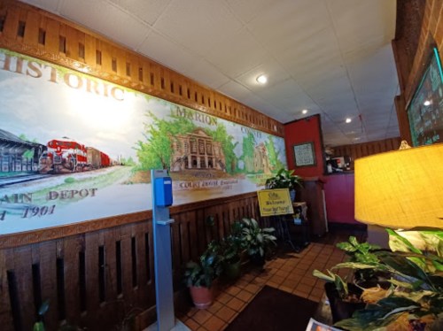 Interior of a restaurant featuring a mural of a historic train depot, plants, and a welcoming sign.
