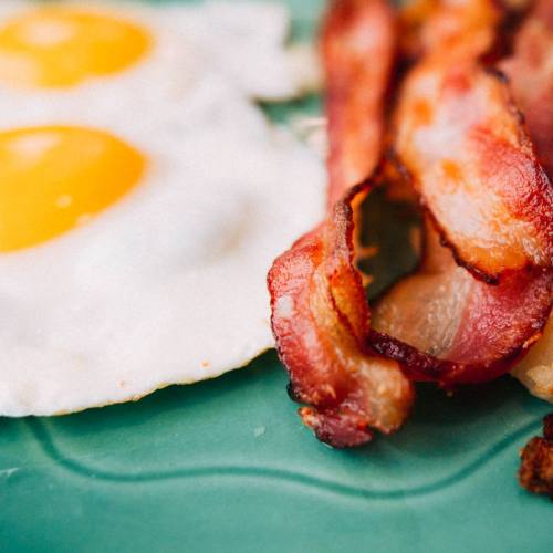 Close-up of two sunny-side-up eggs and crispy bacon on a teal plate.