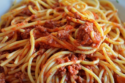 A close-up of spaghetti topped with a rich meat sauce, served in a white bowl.