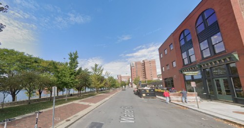 A street view of Water Street lined with trees, buildings, and a clear blue sky. Construction equipment is visible.