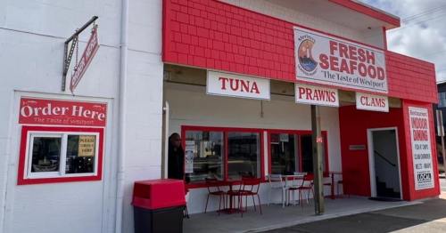 Exterior of a seafood market with a red and white facade, featuring signs for tuna, prawns, and clams. Outdoor seating visible.