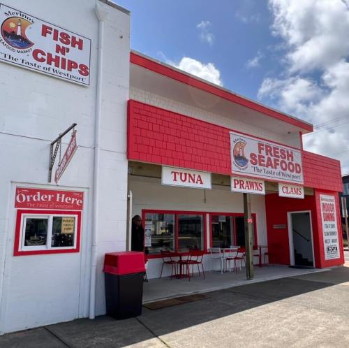 Exterior of a seafood market with signs for fish and chips, fresh seafood, and outdoor seating. Bright red and white colors.