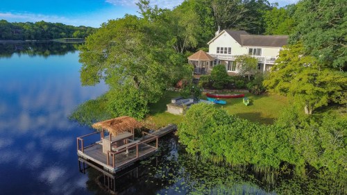 A serene lakeside home with a dock, surrounded by lush greenery and kayaks on the water.