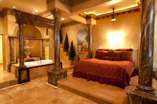 Luxurious bedroom with a marble platform bed, decorative columns, and a spa-like area featuring a fountain and bathtub.