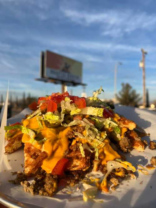 A plate of loaded nachos topped with cheese, lettuce, tomatoes, and ground beef, with a blue sky in the background.