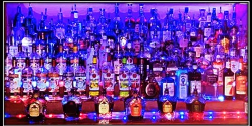 A colorful bar shelf filled with various bottles of liquor, illuminated by vibrant lights.
