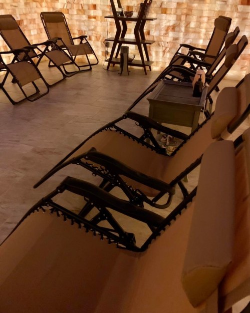 A dimly lit room with several reclining chairs arranged against a salt brick wall.
