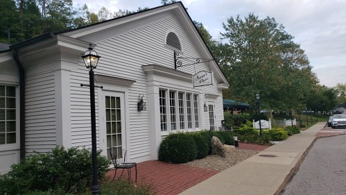 A charming white building with large windows, surrounded by greenery and a brick walkway, on a quiet street.