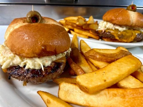 A juicy burger topped with coleslaw and an olive, served with golden fries on a white plate.