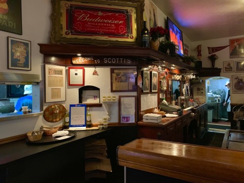 A cozy bar interior with wooden counters, vintage decor, and a welcoming sign reading "Welcome to Scott's."