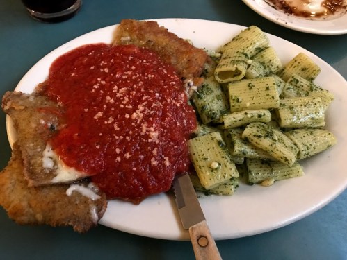 A plate of breaded chicken topped with marinara sauce and grated cheese, served with pesto pasta on the side.