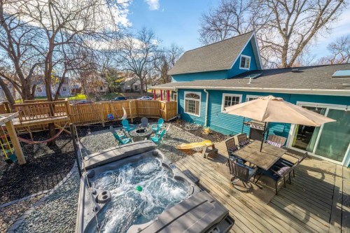 A backyard with a hot tub, patio furniture, and a playground, surrounded by trees and a blue house.