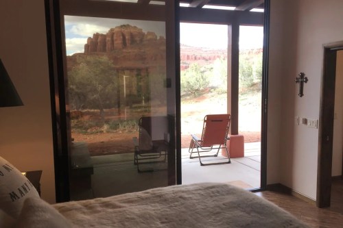A cozy room with a view of red rock formations and greenery through large glass doors. A chair is visible on the patio.