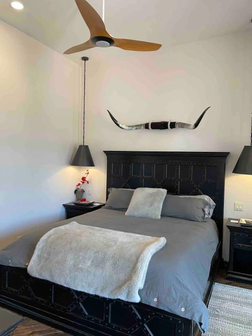 A cozy bedroom featuring a black bed with gray bedding, two pendant lamps, and a decorative longhorn above the headboard.