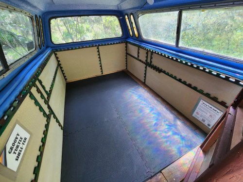 Interior of a van with blue walls, padded flooring, and empty space, featuring signs on the walls.