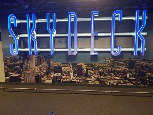 Neon "SKYDECK" sign against a city skyline backdrop, showcasing a vibrant urban landscape.