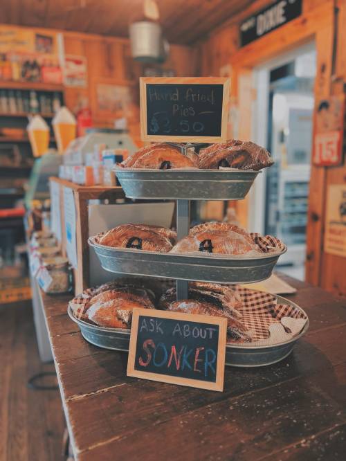 A tiered display of hand-fried pies for sale, with a sign reading "Ask About Sonker" in a rustic shop setting.