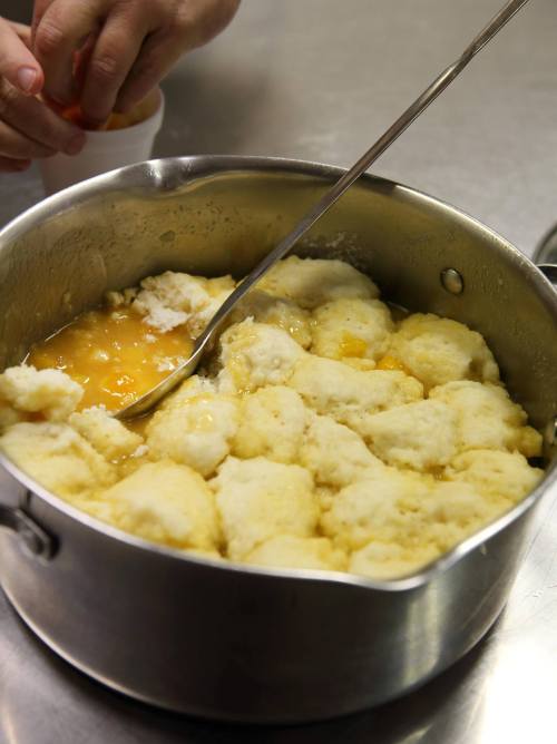 A pot filled with fluffy dumplings in a golden sauce, with a spoon stirring the mixture.