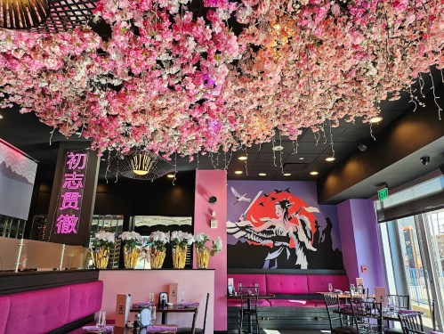 A vibrant restaurant interior with pink floral decor, a mural, and stylish seating. Bright and inviting atmosphere.